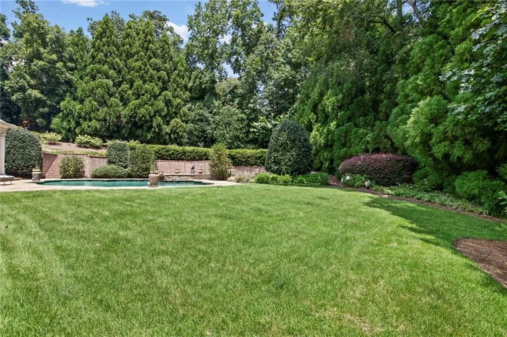 Expansive lawn with a swimming pool, brick retaining walls, and mature landscaping