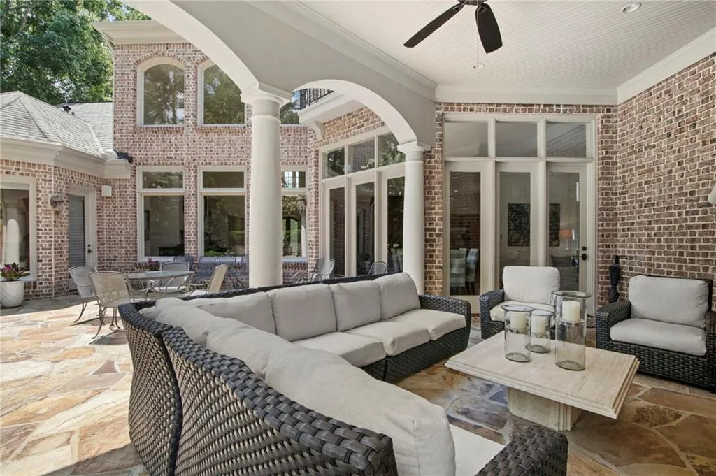 Expansive outdoor living area featuring a flagstone patio, brick exterior, arched portico, and a beadboard ceiling with a ceiling fan