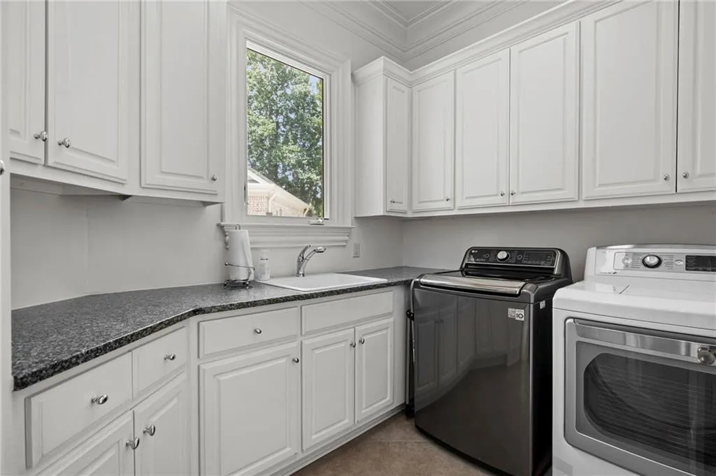White cabinetry with silver-tone hardware, dark speckled countertops, and a single basin sink with a chrome faucet