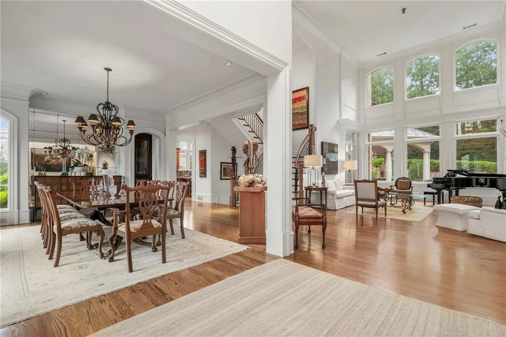 Hardwood flooring throughout, a grand staircase with wood railing, arched and floor-to-ceiling windows, and a formal dining area with a chandelier