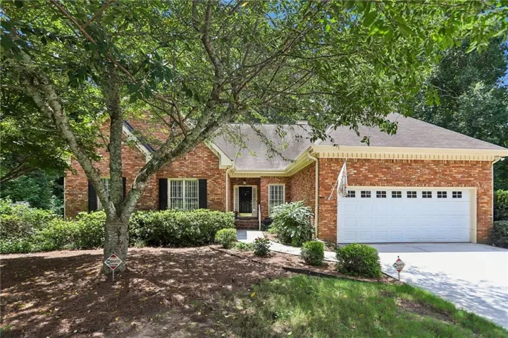 Brick facade residence featuring a two-car garage with transom windows, a covered entry, established landscaping, and a sloped driveway
