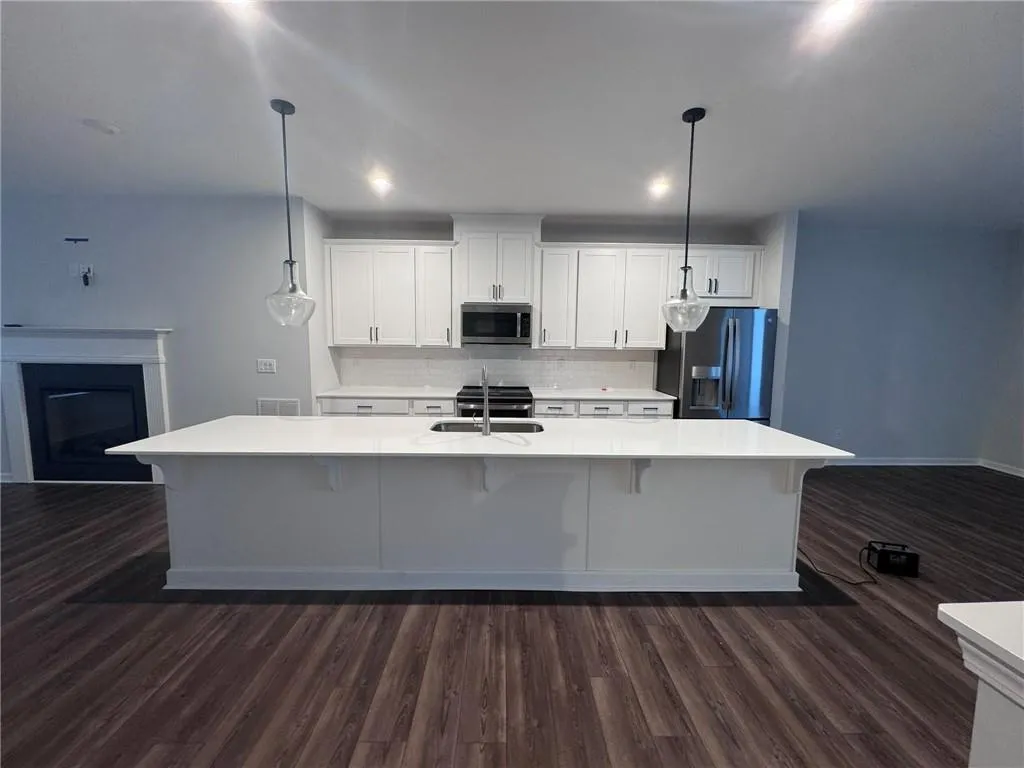 Kitchen featuring a kitchen breakfast bar, white cabinetry, decorative backsplash, stainless steel appliances, and dark wood finished floors