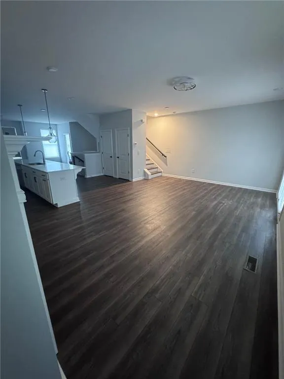 Unfurnished living room with dark wood-style floors and stairway