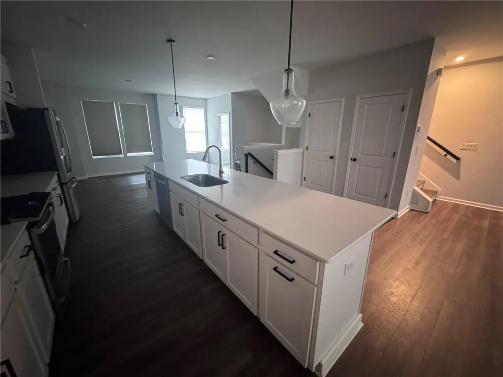 Kitchen featuring white cabinetry, stainless steel appliances, pendant lighting, dark wood-style flooring, and a center island with sink