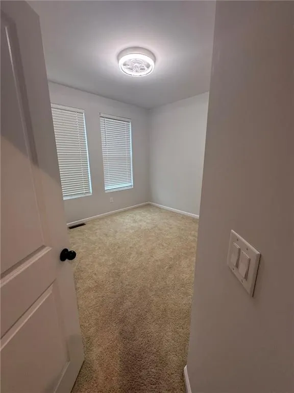 Unfurnished room featuring light carpet and baseboards