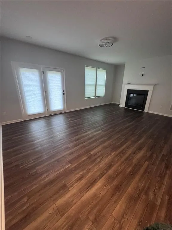 Unfurnished living room featuring a glass covered fireplace and dark wood-style flooring