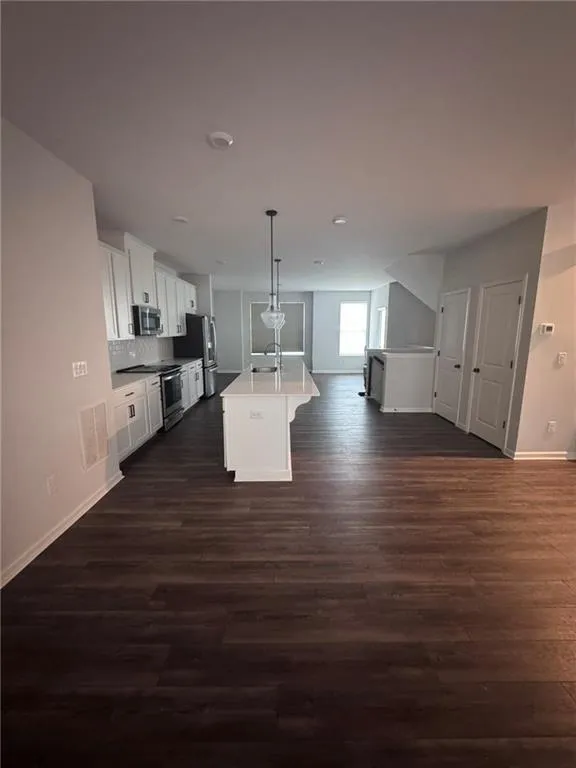 Kitchen featuring white cabinetry, decorative light fixtures, open floor plan, a kitchen island with sink, and appliances with stainless steel finishes
