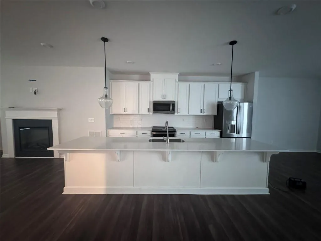 Kitchen with decorative backsplash, white cabinetry, a breakfast bar, appliances with stainless steel finishes, and dark wood finished floors