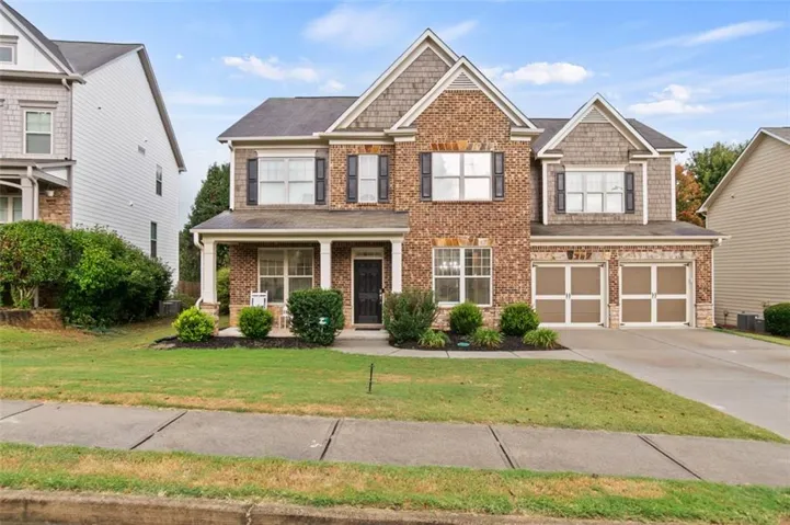 Traditional-style home featuring a brick and shake exterior, a covered front porch with white columns, a two-car garage with frosted-panel doors, and a landscaped front yard