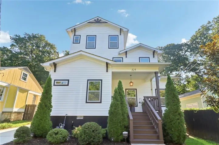 White siding exterior with black trim windows, covered front porch, dark wood-finish steps, and mature landscaping