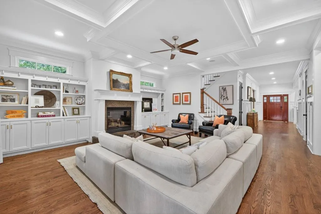 Hardwood flooring, coffered ceiling, built-in shelving, stone-surround fireplace, and a wood entry door with glass panels
