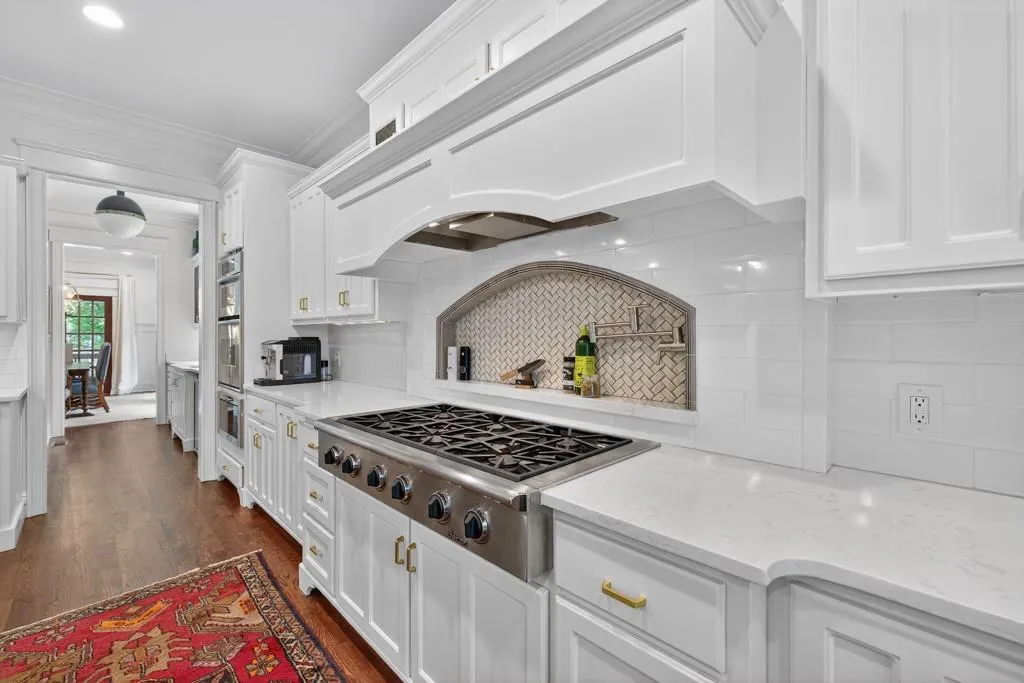 Gourmet kitchen featuring white cabinetry, light-toned countertops, a gas range with a stainless steel hood, built-in double ovens, and wood-finish flooring
