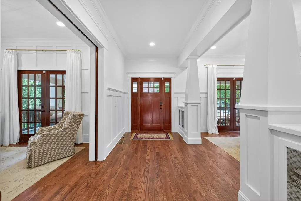 Wood-finish flooring, white paneled walls, recessed lighting, wood-finish entry door with glass panels, and wood-finish French doors