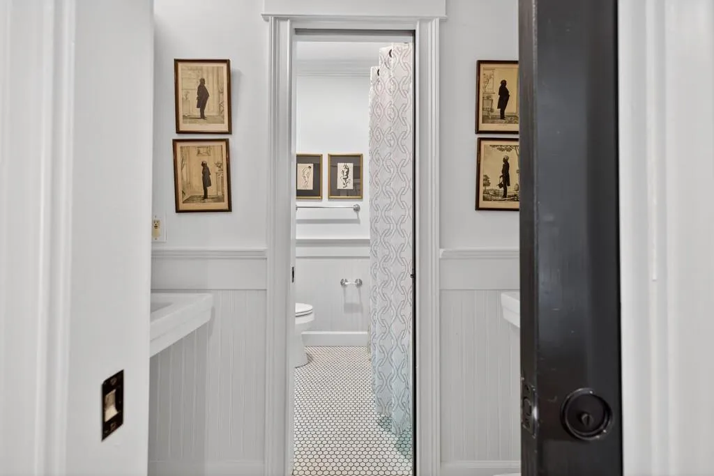 White beadboard wainscoting, white walls, black door, and hexagonal tile flooring