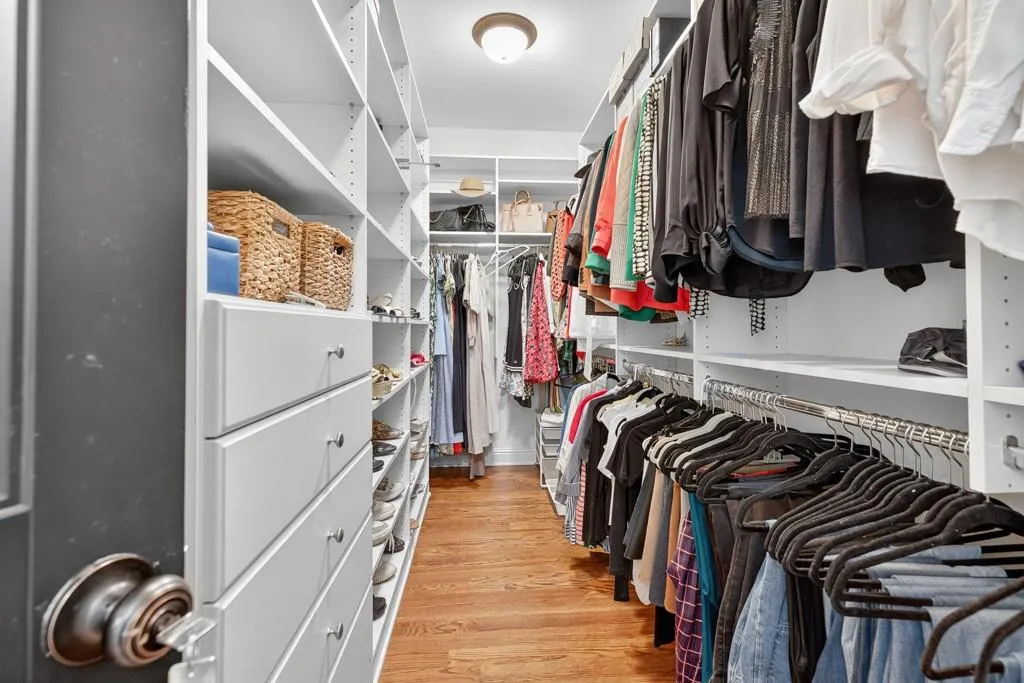 Walk-in wardrobe with extensive custom shelving, integrated drawers, multiple hanging rods, and hardwood flooring