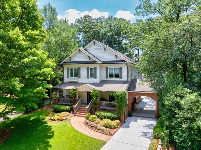 White siding exterior with dark shutters, covered front porch, brick archway, mature landscaping, and a manicured lawn