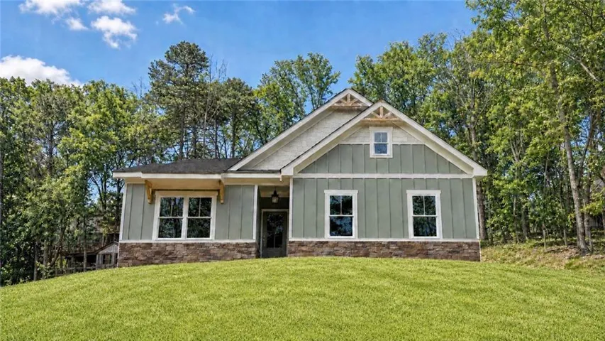 Craftsman-style home featuring a light green siding exterior with stone accents, a dark shingle roof, and white window trim