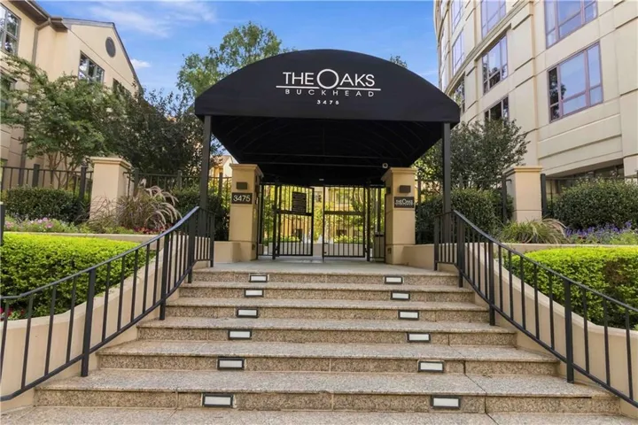 Granite-finish stairs with integrated lighting, wrought iron railings, and a prominent building entrance with a black awning