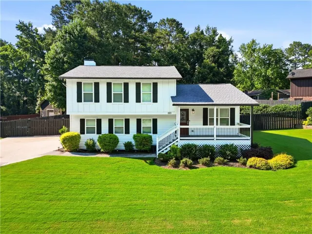 White two-story exterior featuring a covered porch, dark shutters, and a well-maintained front lawn