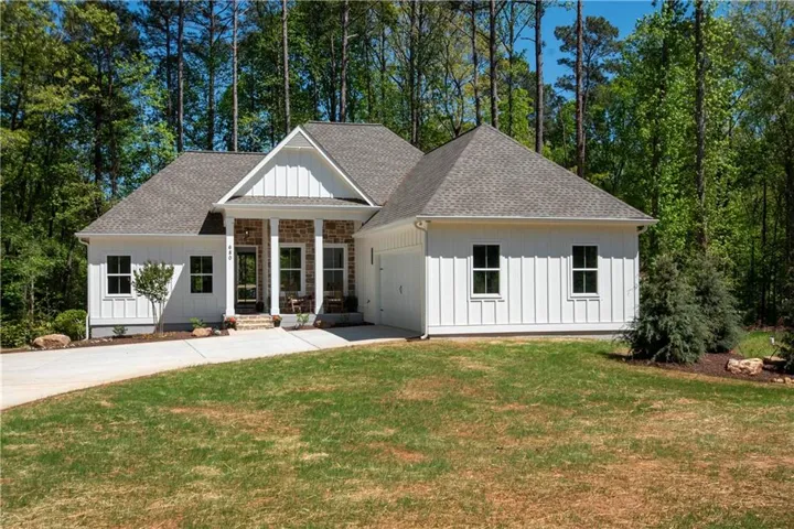 White board-and-batten siding with a stone-clad porch, a prominent gable roof, and an integrated garage