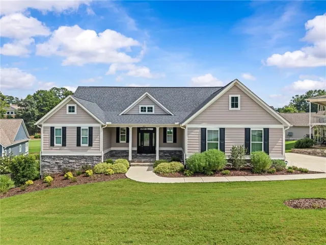 Traditional-style home with a porch, a front lawn, stone siding, and a shingled roof