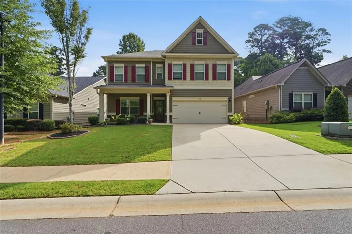 Two-story residential property featuring a covered front porch, red-shuttered windows, a two-car garage, and a concrete driveway