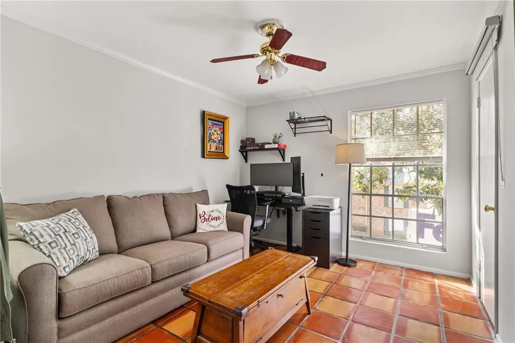 Tiled living area featuring ceiling fan and ornamental molding