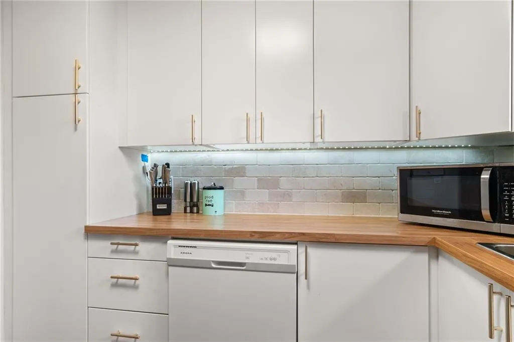 Kitchen with decorative backsplash, stainless steel microwave, white cabinetry, butcher block counters, and dishwashing machine
