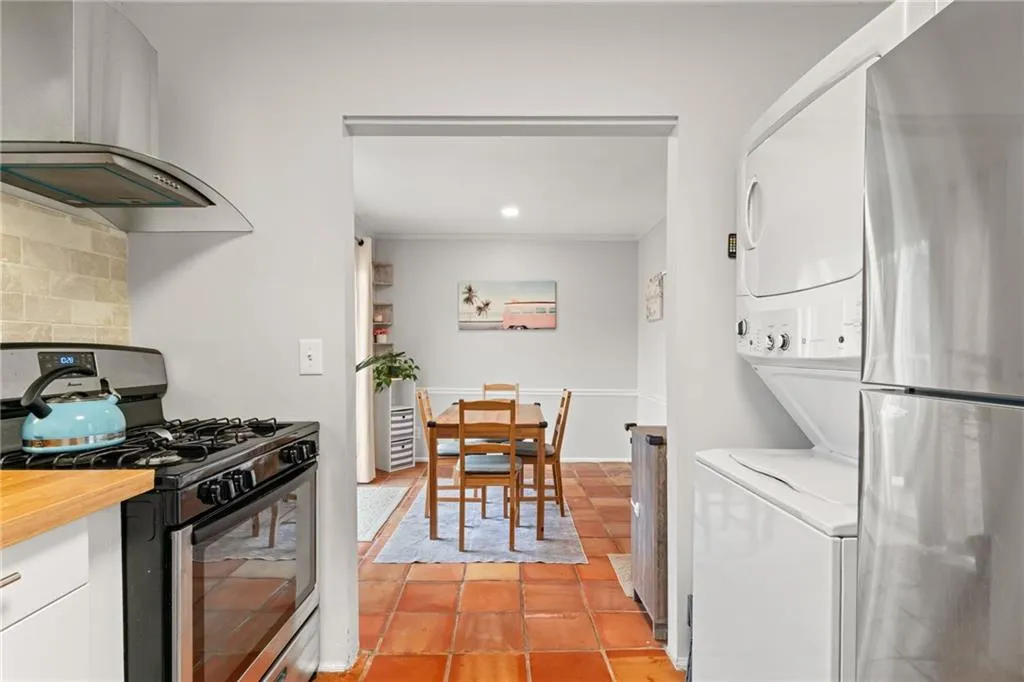 Kitchen featuring extractor fan, stacked washer and dryer, white cabinets, gas range oven, and tasteful backsplash