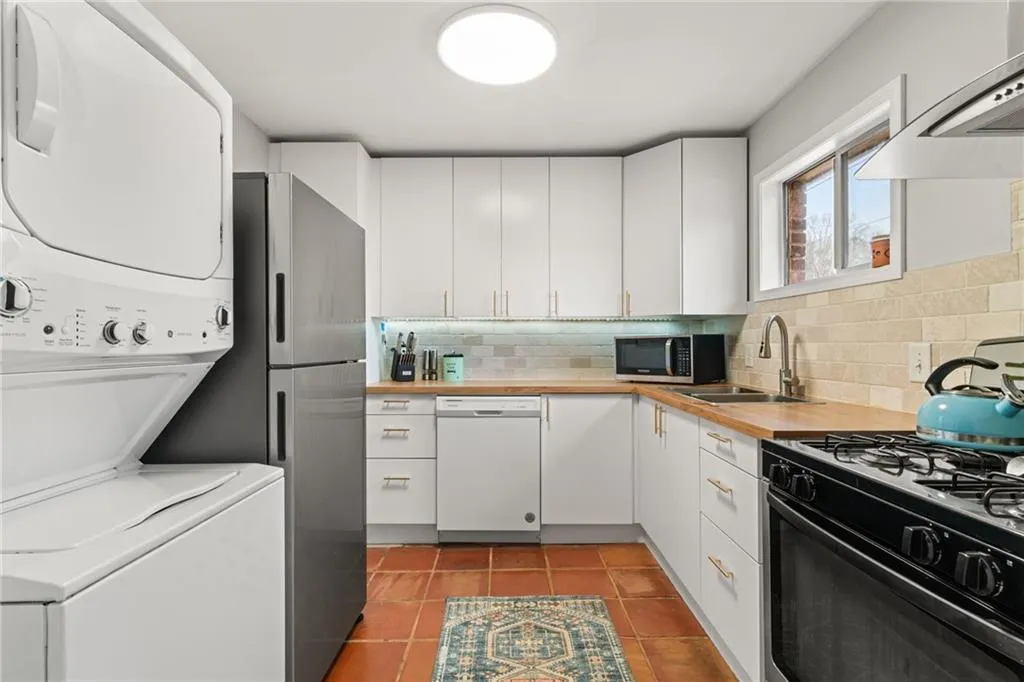 Kitchen featuring stacked washer and clothes dryer, backsplash, stainless steel appliances, wall chimney exhaust hood, and light tile patterned floors