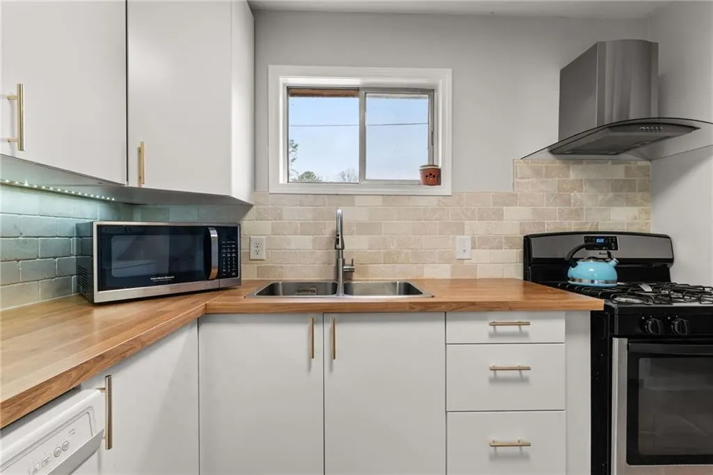 Kitchen featuring a sink, stainless steel appliances, wall chimney exhaust hood, butcher block counters, and white cabinets