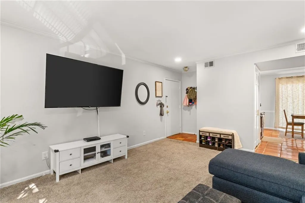 Living room with visible vents, carpet, baseboards, and ornamental molding