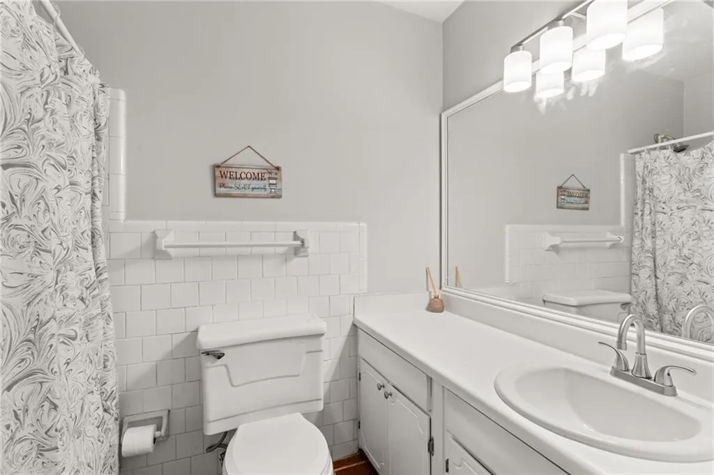 Bathroom featuring tile walls, a wainscoted wall, toilet, a shower with shower curtain, and vanity