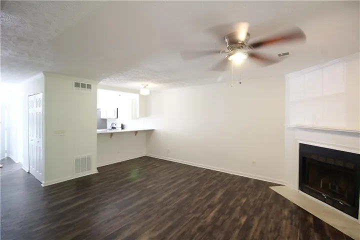 Open-concept living area featuring wood-finish flooring, a white mantel fireplace, and a ceiling fan with integrated lighting