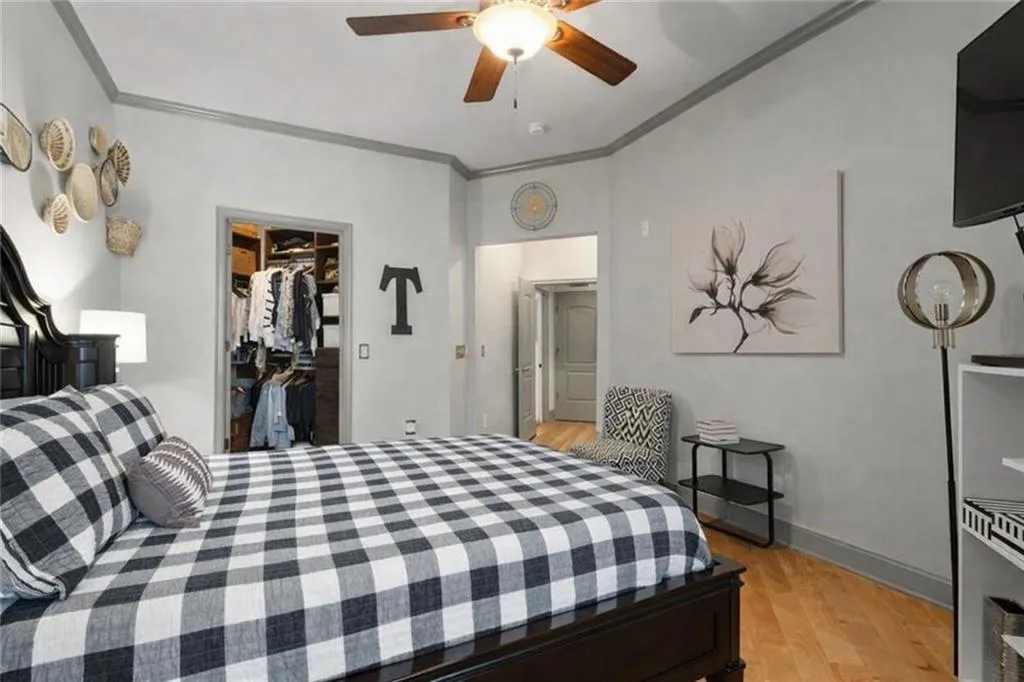 Bedroom with crown molding, light wood finished floors, a walk in closet, and a ceiling fan