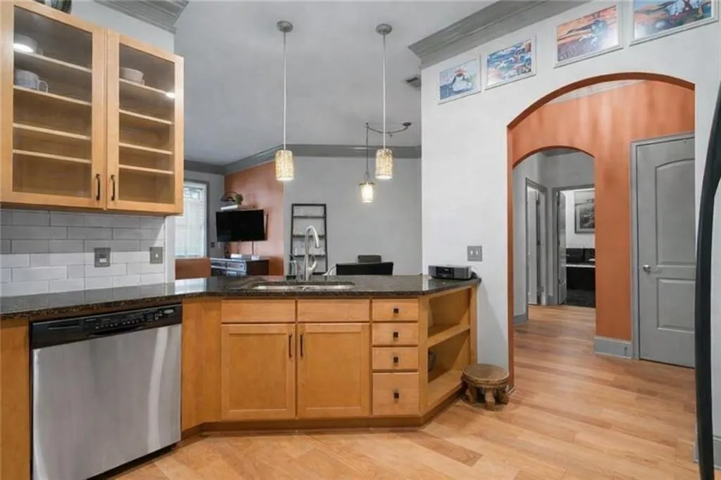 (virtually staged to remove decor) Kitchen featuring stainless steel dishwasher, hanging light fixtures, dark stone countertops, crown molding, and light wood-type flooring