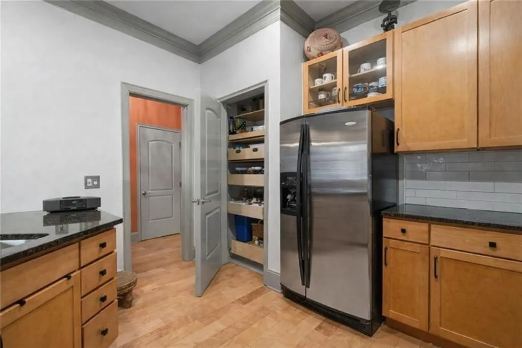 (virtually staged to remove decor) Kitchen with glass insert cabinets, stainless steel fridge, dark stone countertops, light wood-style floors, and ornamental molding