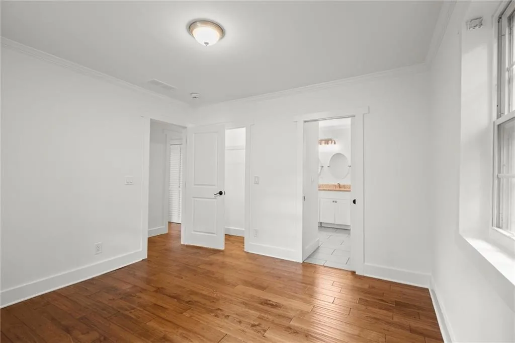 Unfurnished bedroom with wood finished floors, ornamental molding, ensuite bathroom, and a walk in closet