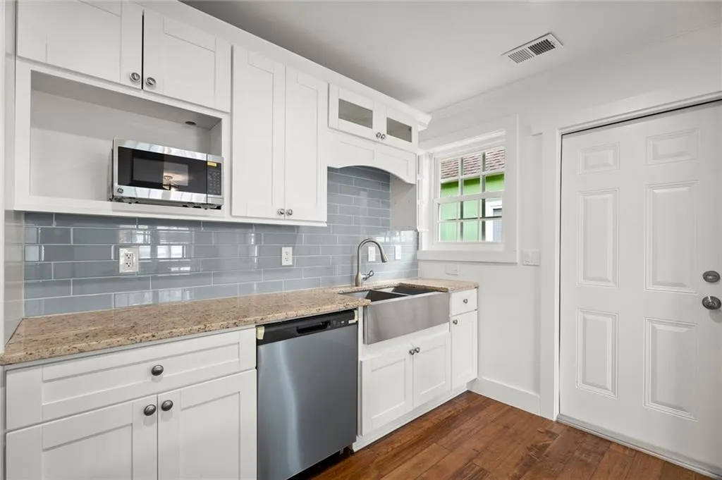 Kitchen featuring stainless steel appliances, dark wood finished floors, backsplash, light stone countertops, and glass insert cabinets