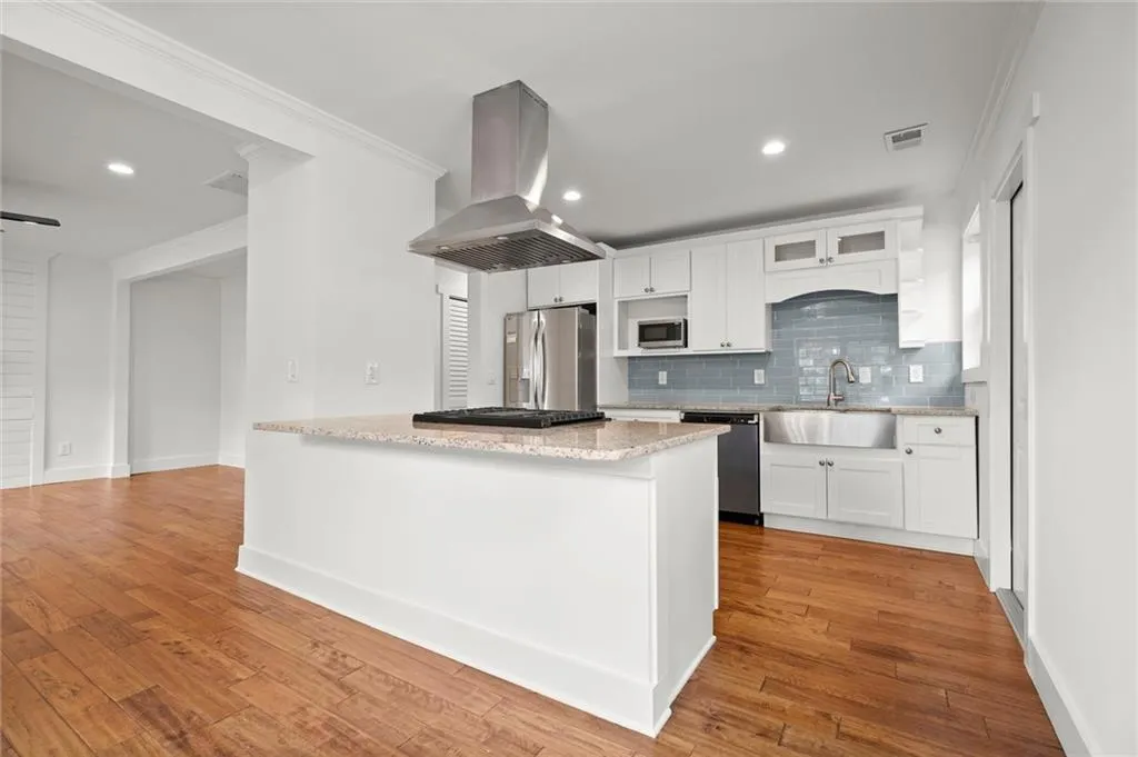Kitchen with island exhaust hood, ornamental molding, tasteful backsplash, light stone counters, and white cabinets