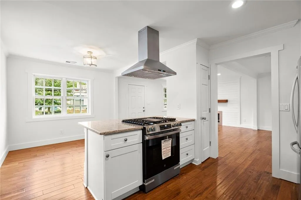 Kitchen with stainless steel range with gas cooktop, island exhaust hood, light stone counters, hardwood / wood-style floors, and ornamental molding