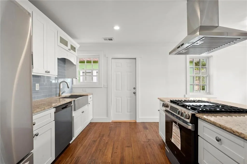 Kitchen featuring appliances with stainless steel finishes, island range hood, dark wood-style floors, glass insert cabinets, and light stone counters