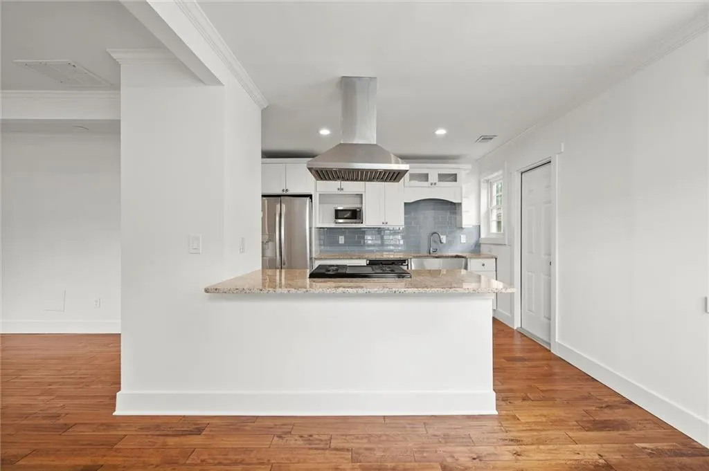 Kitchen featuring island range hood, appliances with stainless steel finishes, a peninsula, white cabinets, and tasteful backsplash
