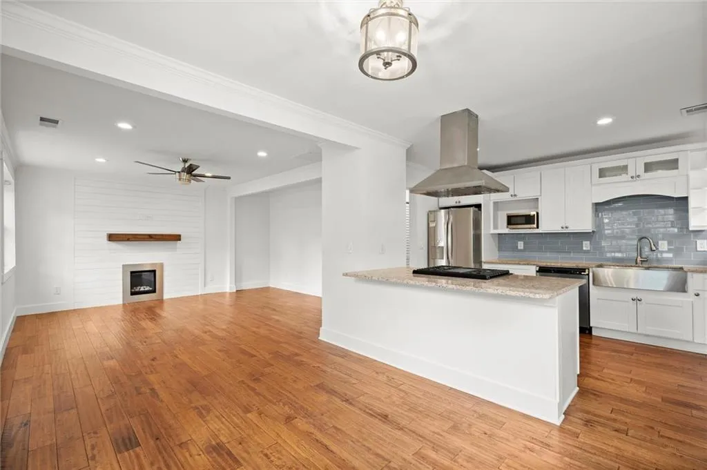 Kitchen with backsplash, island exhaust hood, white cabinets, appliances with stainless steel finishes, and wood finished floors