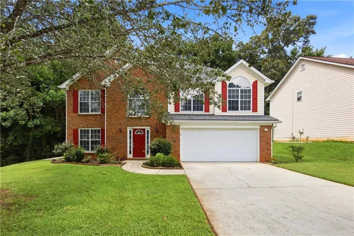Traditional brick-front residence featuring a prominent red entry door, white garage door, and red shutters