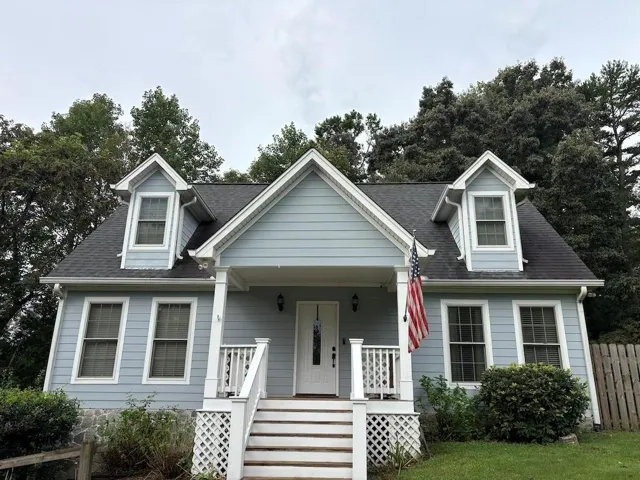 Light blue siding exterior featuring a covered porch, white railing, and dual dormer windows