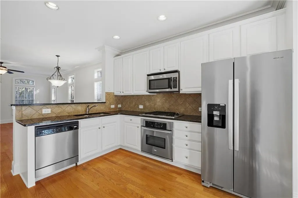 Kitchen with stainless steel appliances, hanging light fixtures, tasteful backsplash, crown molding, and white cabinetry