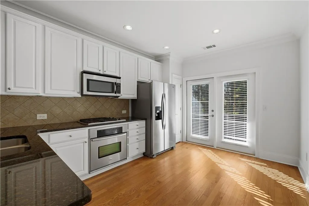 Kitchen with white cabinets, stainless steel appliances, ornamental molding, dark stone countertops, and recessed lighting