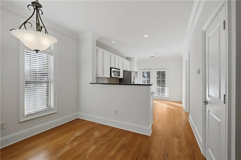Kitchen with crown molding, white cabinetry, light wood finished floors, hanging light fixtures, and a peninsula