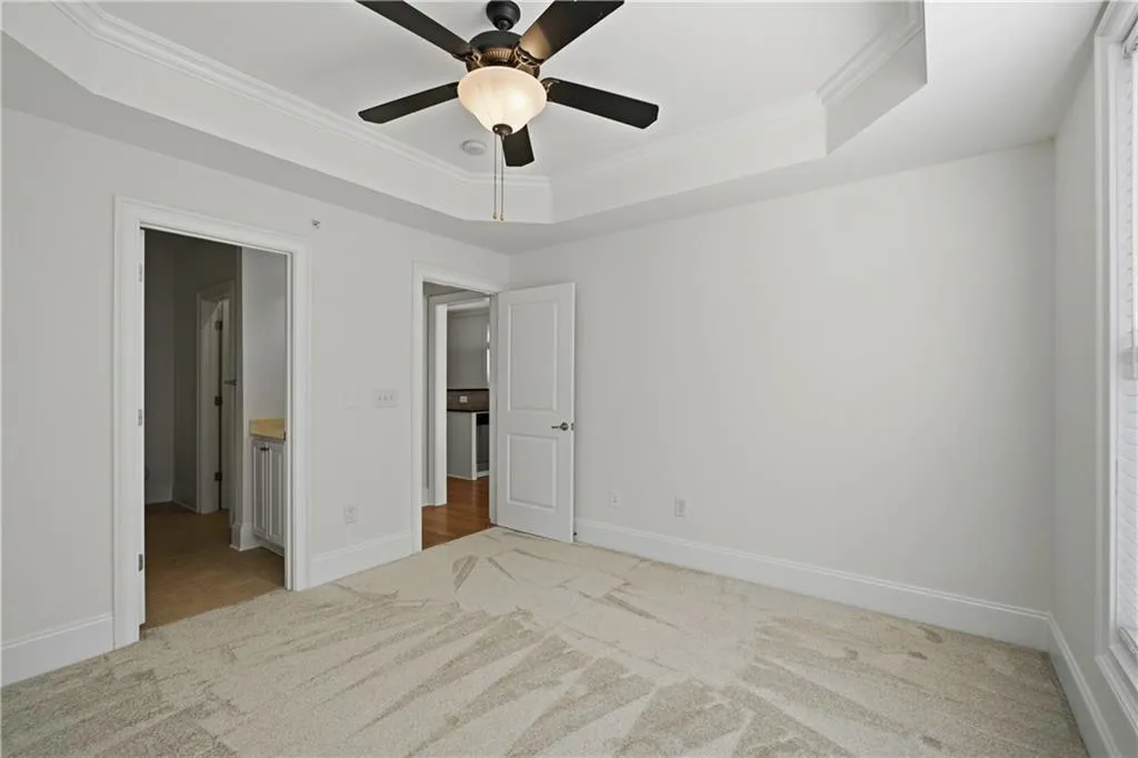 Unfurnished bedroom featuring light colored carpet, ornamental molding, ceiling fan, a tray ceiling, and connected bathroom